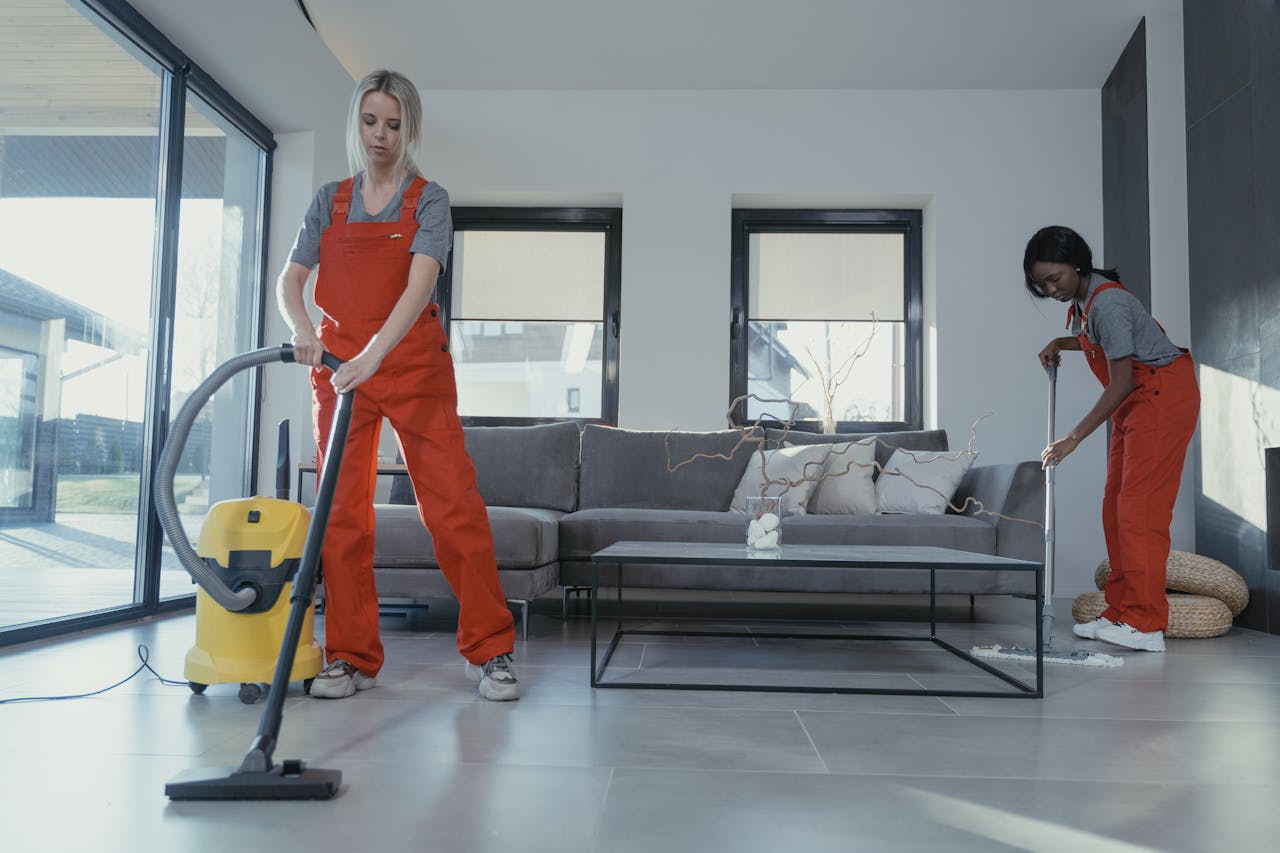 Mastering the First Impression: Your intriguing post title goes here Two women in red overalls vacuuming and sweeping a modern living room.
