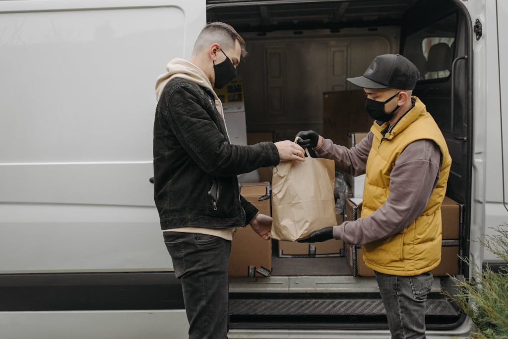 Masked deliveryman hands package to customer from van, ensuring safety and hygiene.