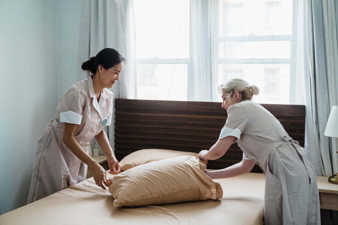 The Art of Drawing Readers In: Your attractive post title goes here Two housekeepers in uniform collaborate while making a bed in a bright, peaceful bedroom.